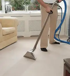 Professional carpet cleaner using a hot-water extraction wand and hose machine in a living room in Allentown, PA.