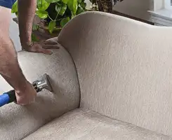 Professional upholstery cleaner deep-cleaning a fabric sofa with a handheld extraction tool and hose in Allentown, PA.